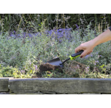 Osoba používá malou zahradní lopatku k hrabání v květinovém záhonu.