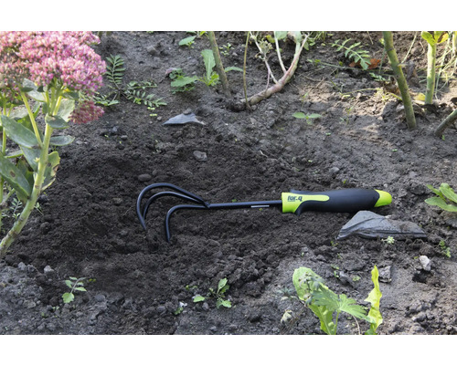 Zahradní hrábě v zemi vedle květiny