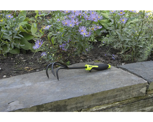 Zahradní kultivátor se třemi hroty a plastovou rukojetí před květinovým záhonem