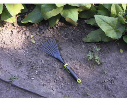 Zahradní hrábě na zahradní půdě s rostlinami