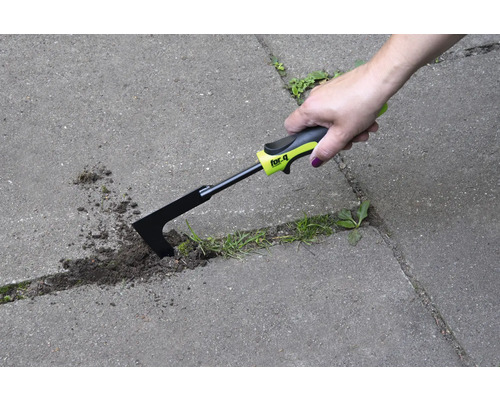 Ruka používá škrabku na spáry k odstraňování plevele mezi dlažebními kameny.