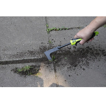 Osoba odstraňuje plevel z dlažby pomocí škrabky na spáry.