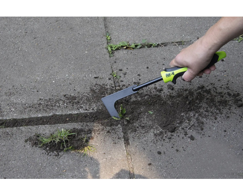 Osoba odstraňuje plevel z dlažby pomocí škrabky na spáry.