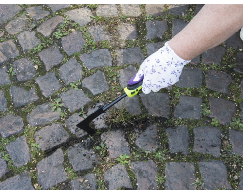 Osoba odstraňuje plevel spárovací škrabkou z dlážděné cesty.