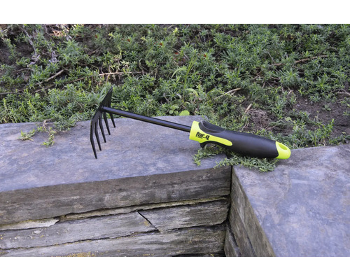 Hrábě na listí a zahradní hrábě s hroty a plastovou rukojetí na kamenné zdi