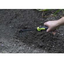 Ruka drží malou motyku v zahradní půdě