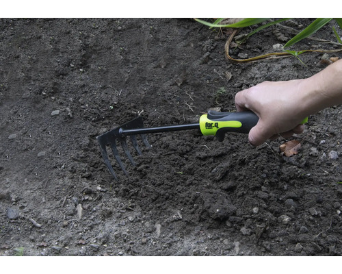 Ruka drží malou motyku v zahradní půdě