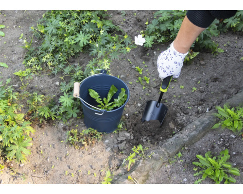 Osoba odstraňuje plevel lopatkou ze zahrady, plevel se sbírá do kbelíku