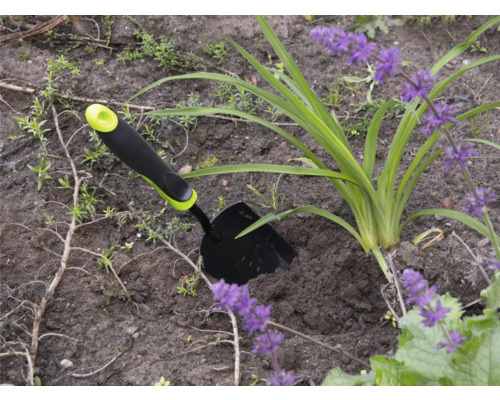 Zahradní scéna s malou zahradní lopatkou vedle rostliny s fialovými květy.