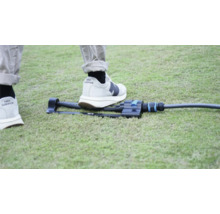 Zahradní zavlažovač na trávníku s nohou pro srovnání velikosti.