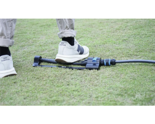 Zahradní zavlažovač na trávníku s nohou pro srovnání velikosti.