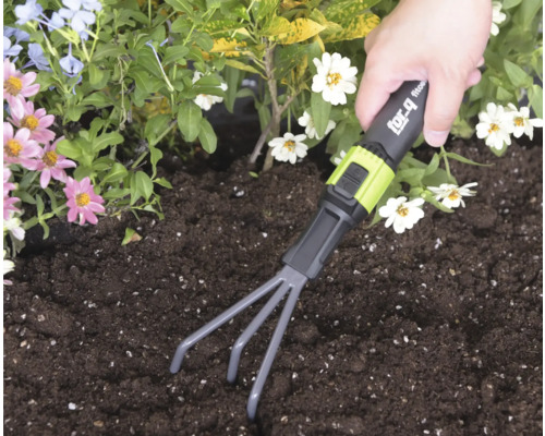 Ruka používá ruční hrabičky for_q v tmavé půdě v záhonu s květinami.