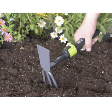 Ruka používá ruční motyčku for_q se zuby a listem v tmavé půdě vedle květin ke kypření země.