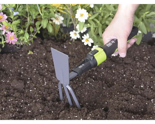 Ruka používá ruční motyčku for_q se zuby a listem v tmavé půdě vedle květin ke kypření země.