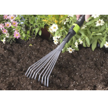 Ruční malé vějířové hrábě for_q používané v tmavé zahradní zemině vedle růžových a bílých květin.