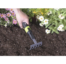 Ruční hrabičky s černo-zelenou rukojetí a for_q Logo používané v tmavé zemině mezi růžovými a bílými květy.