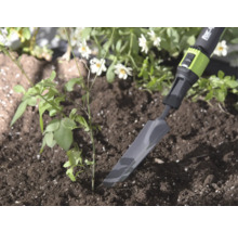 Úzká kovová sázecí lopatka for_q v hlíně vedle malé rostliny, světlé a přírodní zahradní prostředí.