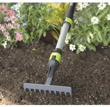 Malé zahradní hrábě s šedou kovovou hlavou a nastavitelnou teleskopickou násadou v zemině před květinami.