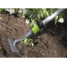 Zahradní plečka s šedou čepelí a zelenou spojkou při odstraňování plevele v tmavé půdě u rostliny.