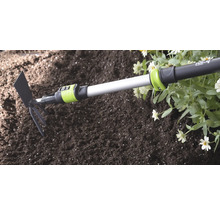 Kombinované zahradní nářadí for_q s teleskopickou násadou v půdě vedle květin.