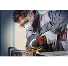 Řemeslník pracuje s akumulátorovou úhlovou bruskou Einhell na kovu s jiskrami, má ochranné brýle, respirátor, ochranu sluchu a rukavice.