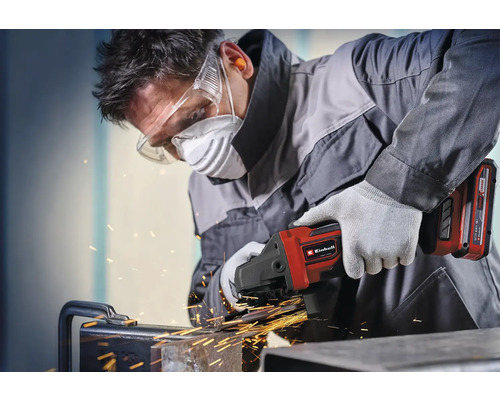 Řemeslník pracuje s akumulátorovou úhlovou bruskou Einhell na kovu s jiskrami, má ochranné brýle, respirátor, ochranu sluchu a rukavice.