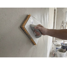 Ruka používající houbové hladítko na čerstvé omítce.