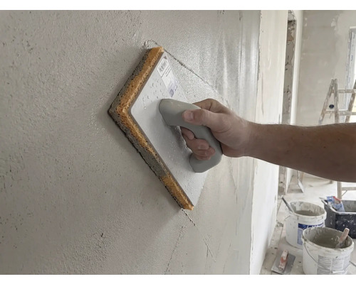 Ruka používající houbové hladítko na čerstvé omítce.