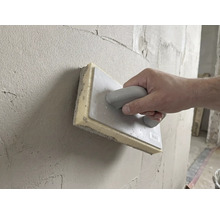 Ruka používá houbové hladítko 28 krát 14 centimetrů k vyhlazování čerstvé omítky na stěně.