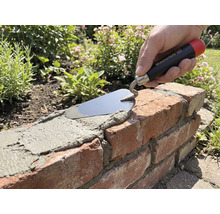 Ruka se zednickou lžící Maurerlob nanáší maltu na cihlovou zídku v zahradě.