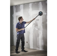 Muž brousí sádrokartonovou stěnu pomocí brusky na sádrokarton s teleskopickou tyčí.