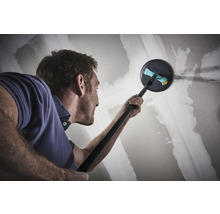 Muž brousí sádrokartonovou stěnu teleskopickou bruskou.