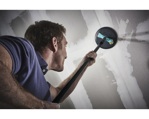 Muž brousí sádrokartonovou stěnu teleskopickou bruskou.