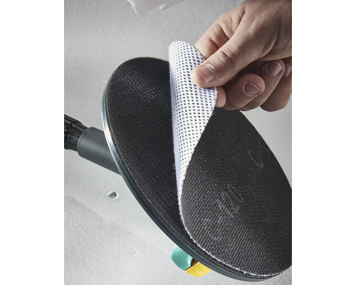 Ruka připevňuje bílý mřížkový brusný kotouč na černý kulatý brusný talíř brusky na sádrokarton.