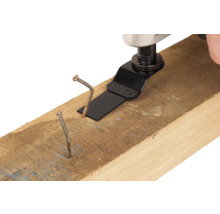 Multifunkční nářadí s pilovým listem řeže hřebík v dřevěném trámu.