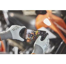 Osoba má na sobě pracovní rukavice s dotykovou funkcí a chytrým telefonem fotografuje motocykl v dílně.