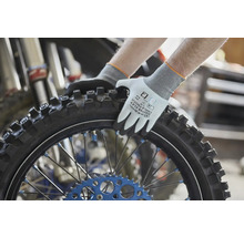 Pracovní rukavice Gebol Master Flex Cool a Touch držící motocyklovou pneumatiku s drapáky v dílně.