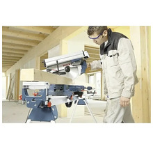 Řemeslník řeže dřevěný trám kapovací a pokosovou pilou Bosch na pracovním stole na světlé stavbě.