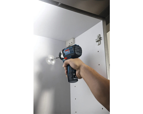 Akumulátorový rázový utahovák Bosch při šroubování vrutu do bílé skříně.