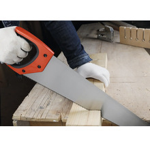 Osoba řeže dřevěný hranol ruční pilou na pracovním stole v jasné dílně.