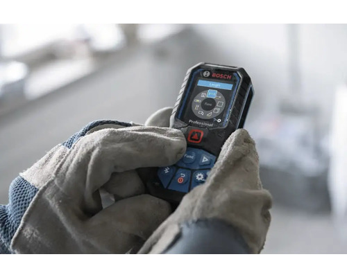 Laserový dálkoměr Bosch Professional ovládaný rukama v pracovních rukavicích, digitální displej s funkcemi měření.