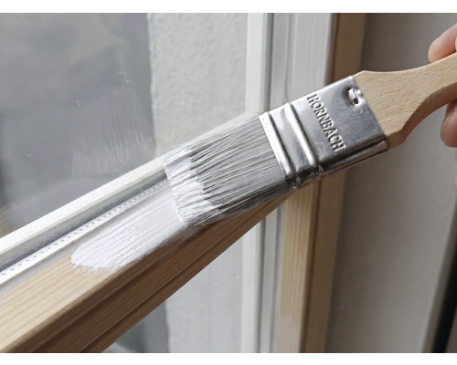 Plochý štětec Hornbach nanášející bílou barvu na dřevěný okenní rám.
