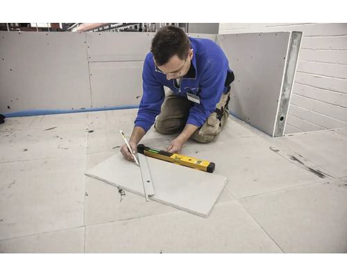 Řemeslník značící sádrokartonovou desku tužkou a pravítkem vedle digitální vodováhy.