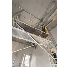 Řemeslník na pojízdném lešení Layher při instalaci na betonovém stropě v hrubé stavbě.