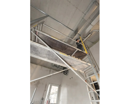 Řemeslník na pojízdném lešení Layher při instalaci na betonovém stropě v hrubé stavbě.