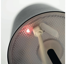 Detail svítidla se zapojeným nabíjecím kabelem USB a svítícím indikátorem nabíjení.