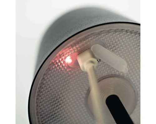 Detail svítidla se zapojeným nabíjecím kabelem USB a svítícím indikátorem nabíjení.