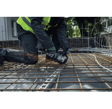 Stavební dělník řeže akumulátorovou úhlovou bruskou Metabo ocelovou výztužnou síť na staveništi.