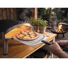 Čerstvě upečená pizza se vyjímá z přenosné pece na pizzu na dřevěném stole na zahradě pomocí lopaty na pizzu s Tenneker Logo.