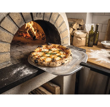 Čerstvě upečená pizza na lopatě na pizzu s Tenneker Logo před hořící kamennou pecí v rustikální kuchyni.